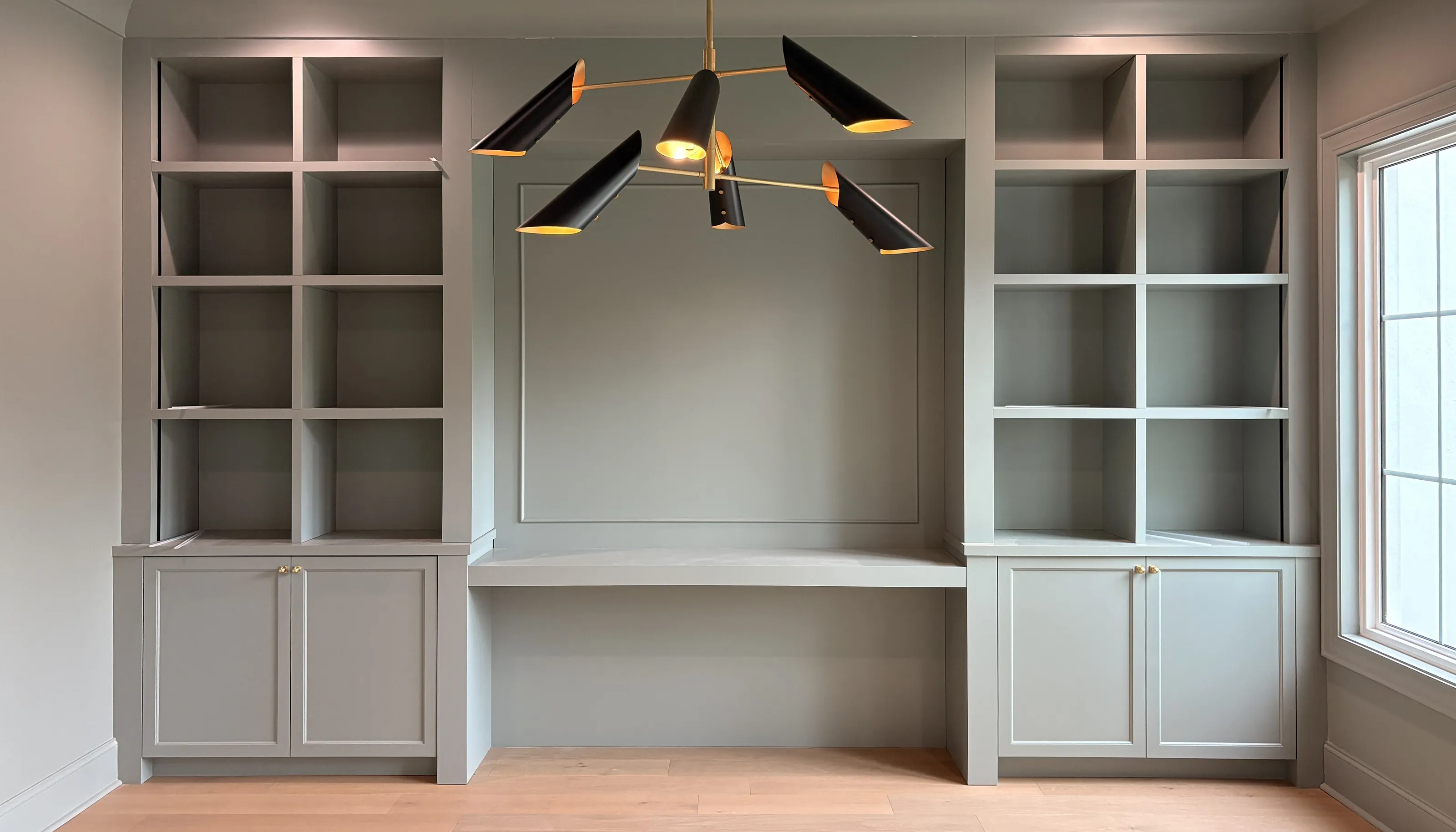 Built in desk between two shelving towers under a black and brass chandelier