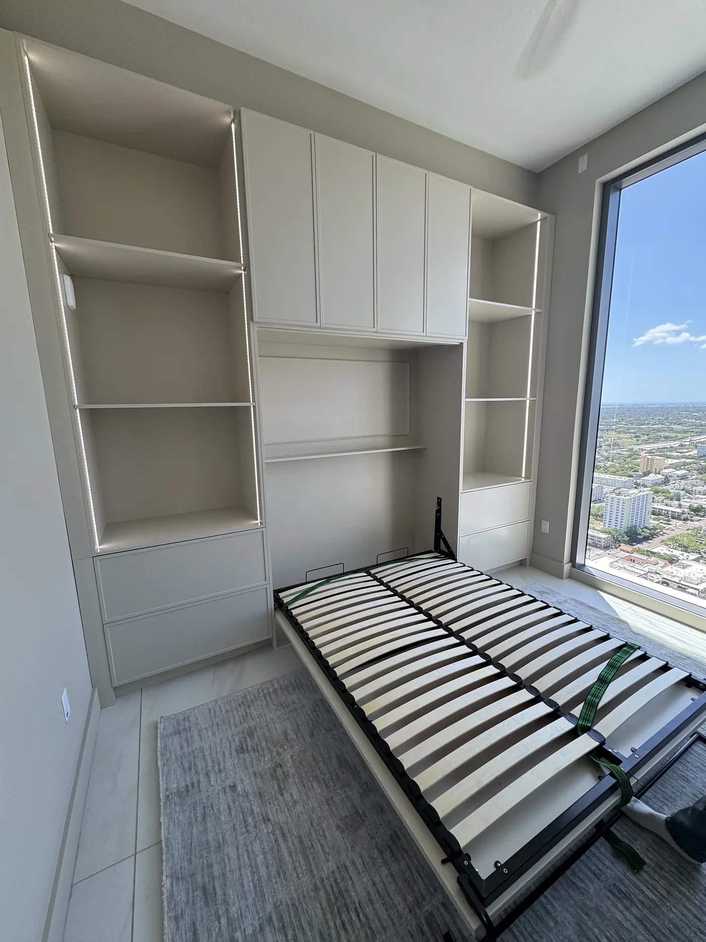 Murphy bed folded down between built in shelving in a room with a city view